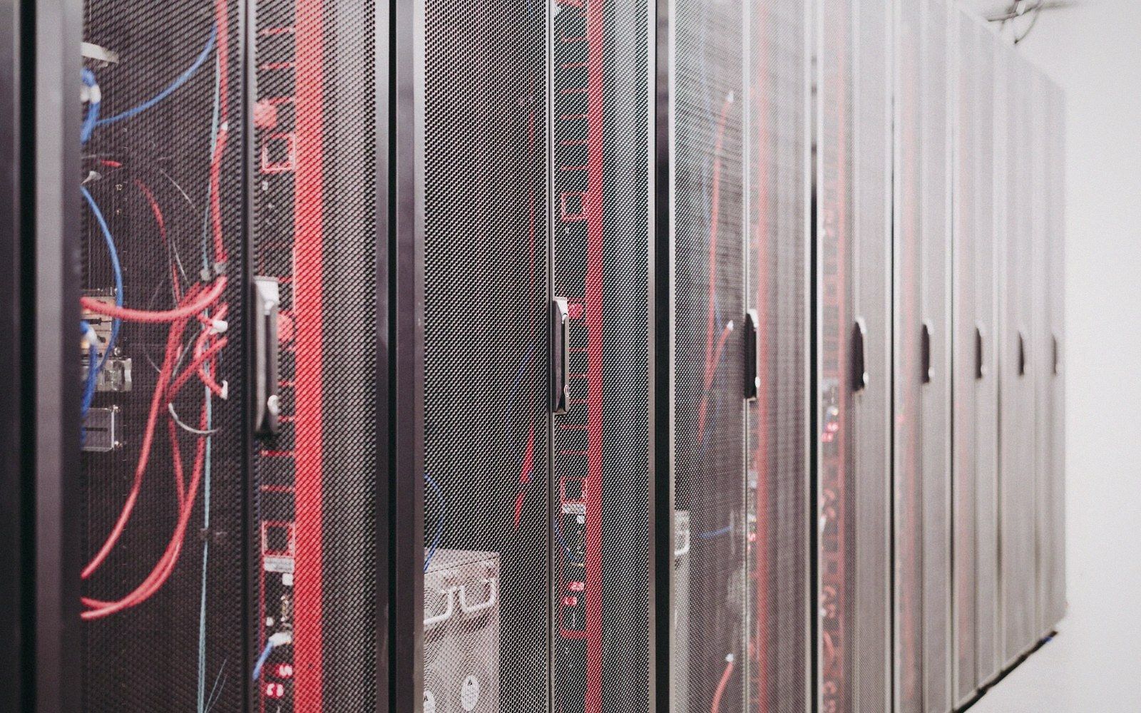 A row of server racks with red and blue cables visible through mesh doors
